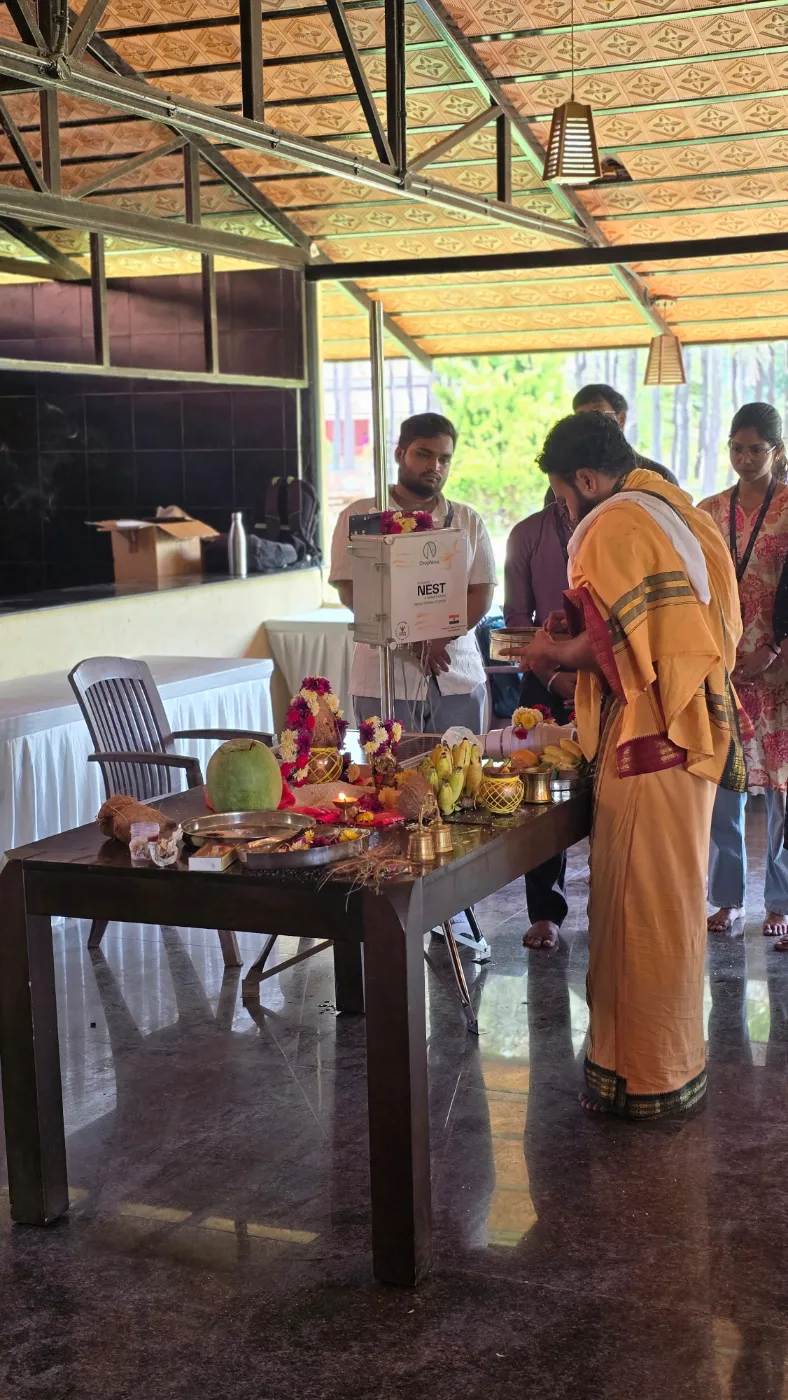 A priest performing a puja at a table of offerings, with a NEST unit behind