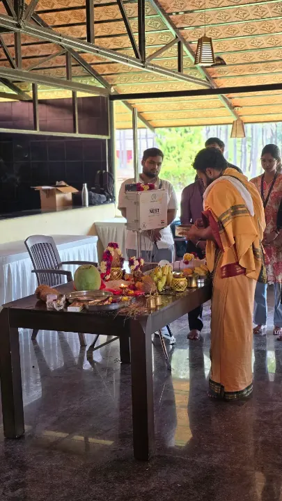 A priest performing a puja at a table of offerings, with a NEST unit behind