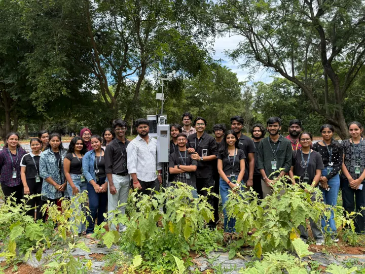 A large group of students standing behind crops around a NEST station