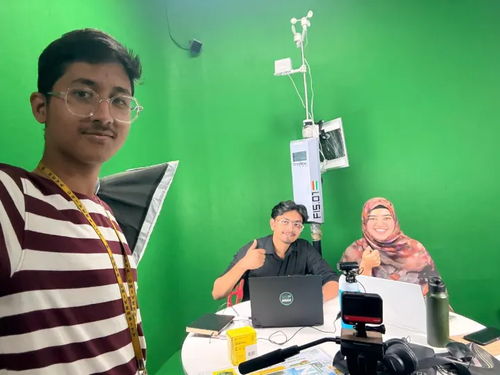 A team member's selfie in a green-screen studio with NEST and two colleagues at a table