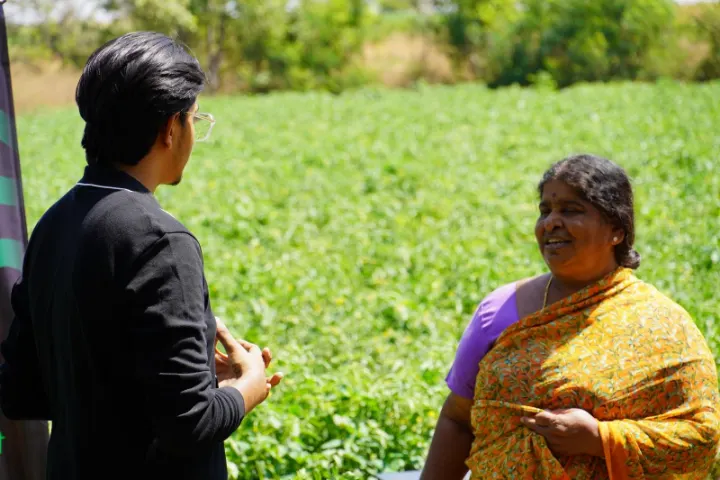 A team member listening to a woman farmer in a green field